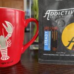 a bag of Addictive Coffee next to a coffee mug with a lobster on it