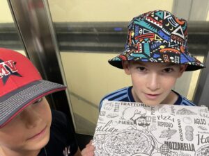 Boys, in the elevator, happily bringing home leftover pizza for dinner