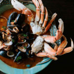Taylor Shellfish Cioppino Kit cooks up to this – Crab and mussels emerging from a tomato -based sugo in a pale blue bowl