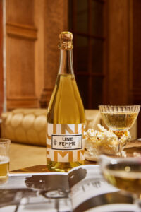 Une Femme_The Betty sparkling wine bottle behind a wavy coupe and a golden background