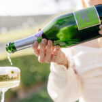 A woman tipping sparkling wine from Fair La Fete into a champagne glass