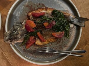 whole roasted branzino on a gray plate topped with blood orange segments and basil