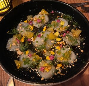 scallop ceviche pieces topped with fruit and herbs on a black plate