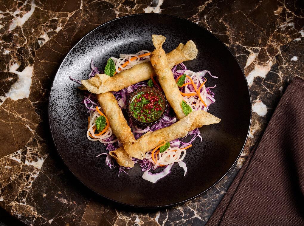 AYA shrimp and crab lumpia form a square with sauce in the middle and on a black plate