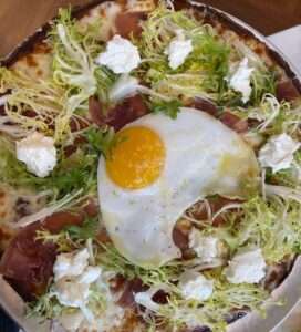 pizza with frisee, dabs of goat cheese and a big duck egg in the middle 