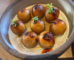 8 toasty balls of sweet potato mochi topped with salsa macha in a grey bowl at Octavia restaurant