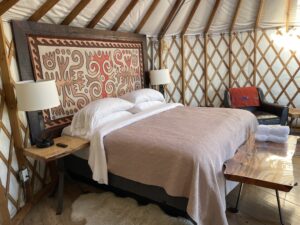 a dressed bed with headboard, side tables with lamps, and bench inside a yurt at glamping site, Treebones, Big Sur