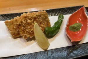 fish breaded in crushed rice crackers with a wedge of lime and a shishito pepper at Yuji restaurant, San Francisco