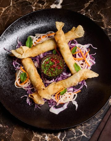 AYA shrimp and crab lumpia form a square with sauce in the middle and on a black plate